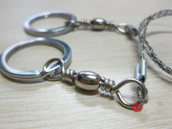 Close-up of a coiled stainless steel survival wire saw with metal pull rings on a wooden background.