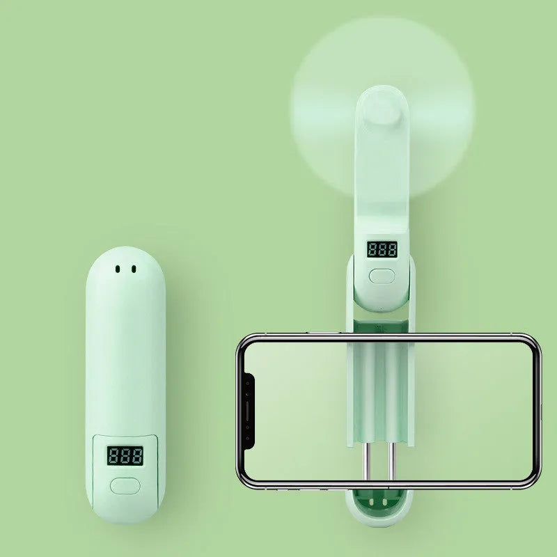 Folded and unfolded views of a green portable mini USB rechargeable fan on a table.