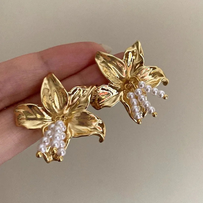 A pair of exaggerated gold metal flower earrings with pearls, showing niche style design.