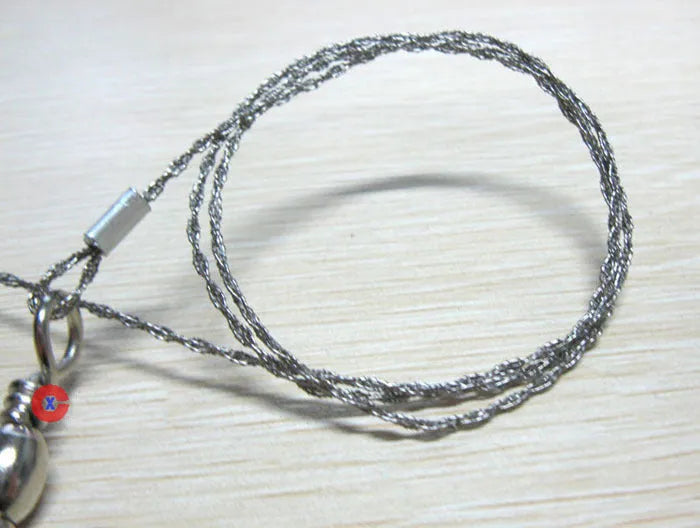 Close-up of a coiled stainless steel survival wire saw with metal pull rings on a wooden background.