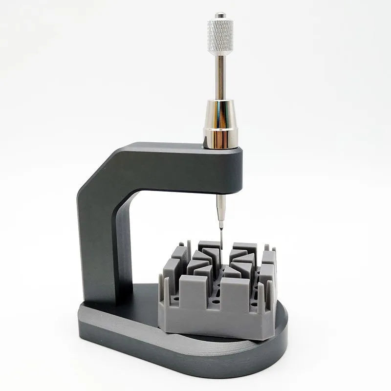 Silver tool steel multi-purpose press strap removal tool for watches and electronics on a workshop surface.