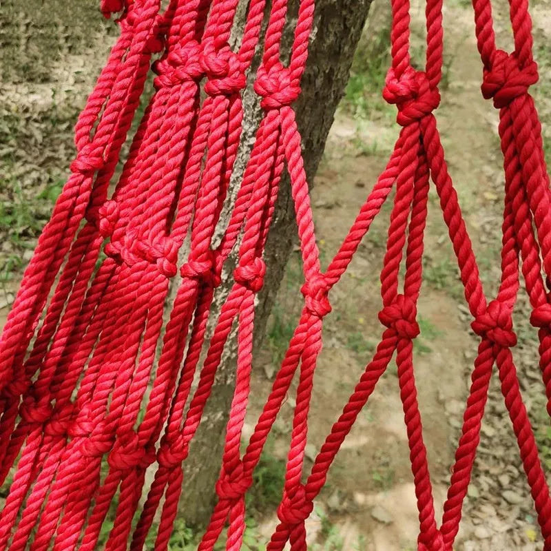 Nylon rope mesh hammock hung between two trees with tying rope visible