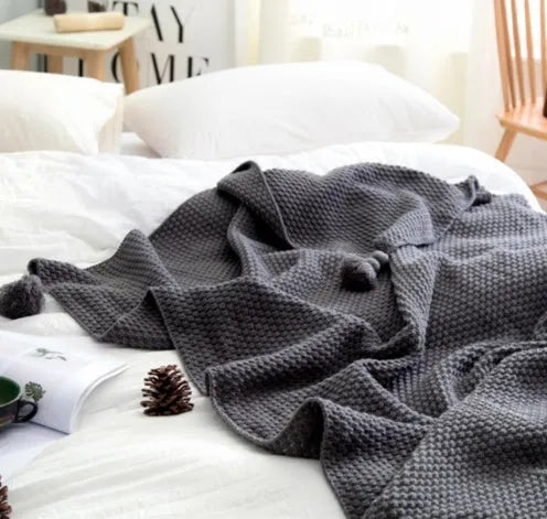 Acrylic knitted blanket with fringed edges in a neutral colour on a sofa.