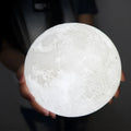 3D printed moon lamp glowing on a wood stand, showing detailed crater texture.