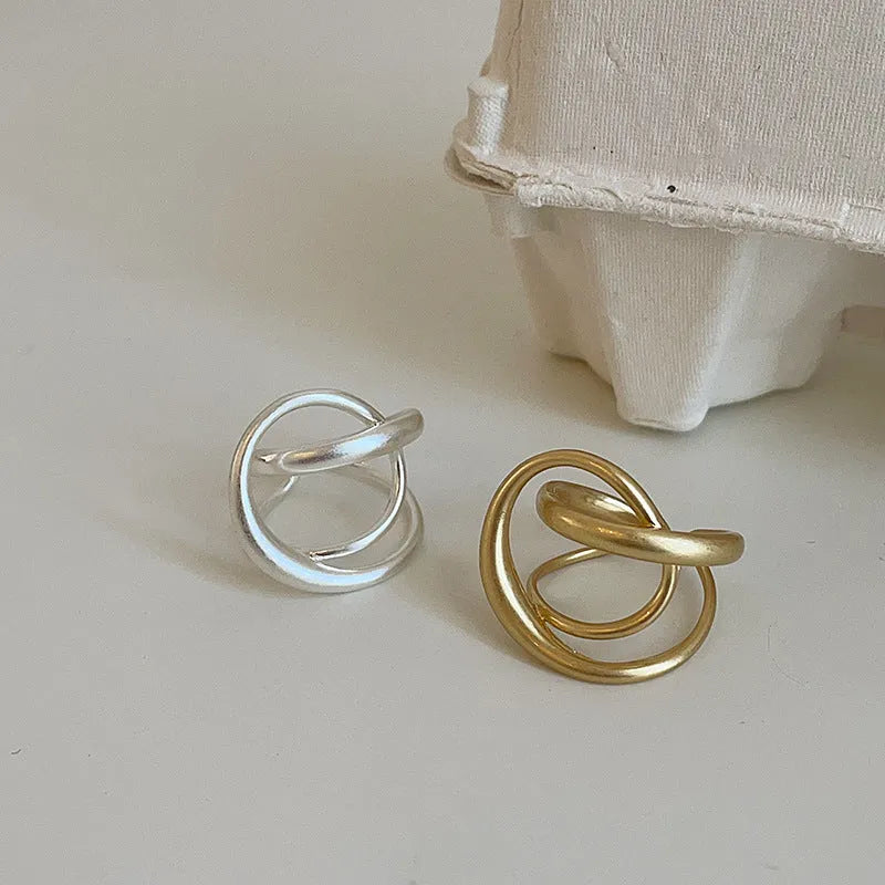 Matte metal open ring with three-dimensional interlaced geometric design in gold or silver finish.