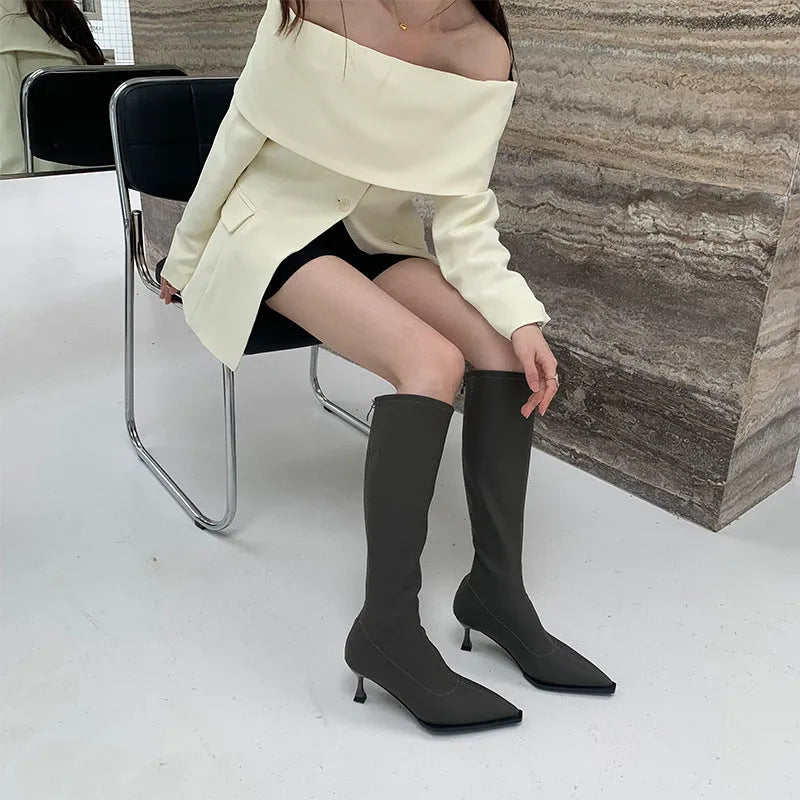 Black pointed toe below knee boots with stiletto heel and back zipper on woman's leg