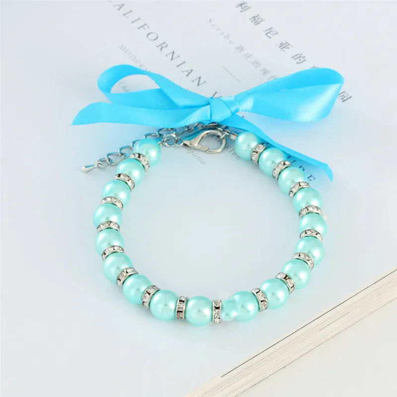 Small dog wearing a blue adjustable pearl and rhinestone necklace with a ribbon bow.