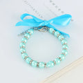 Small dog wearing a blue adjustable pearl and rhinestone necklace with a ribbon bow.