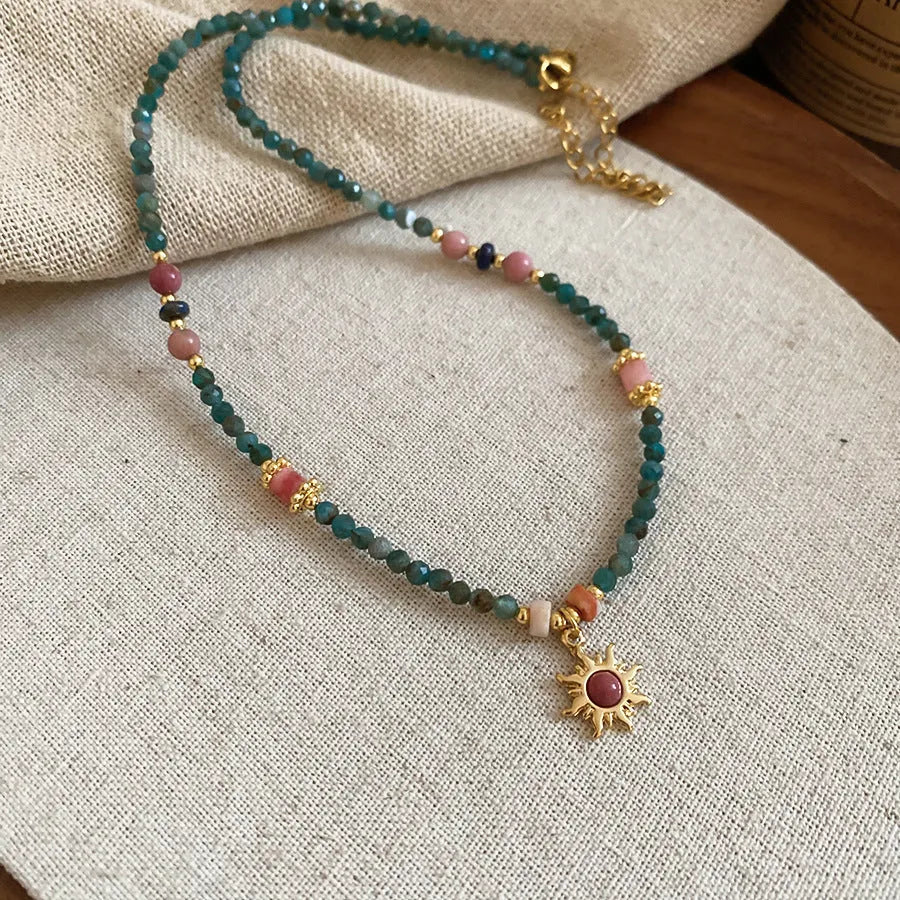 Close-up of a freshwater pearl and geometric stone sun necklace on an adjustable clavicle chain.