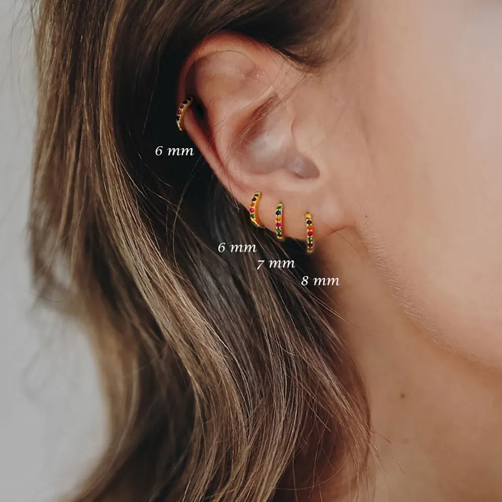 Gold, rose gold, and silver coloured geometric perforated circle stud earrings with zircon details on a white background.