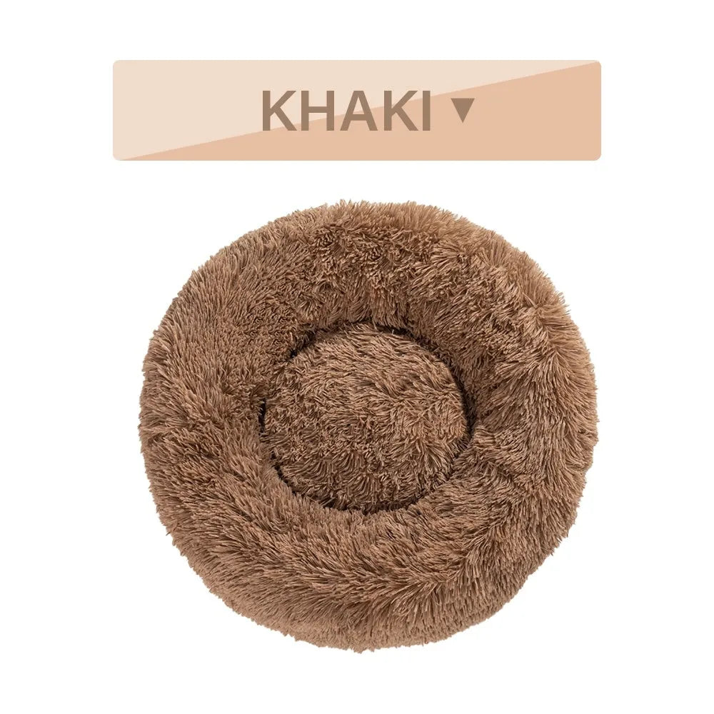 Fluffy donut-shaped dog bed in long plush material, shown in a light grey colour with a raised edge.