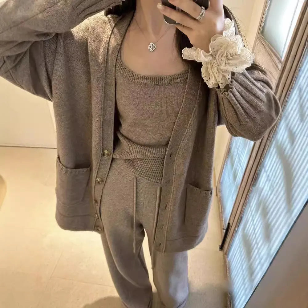 Women's beige knitted cardigan three-piece set with sleeveless vest and suspender trousers on a hanger.