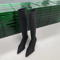 Black pointed toe below knee boots with stiletto heel and back zipper on woman's leg