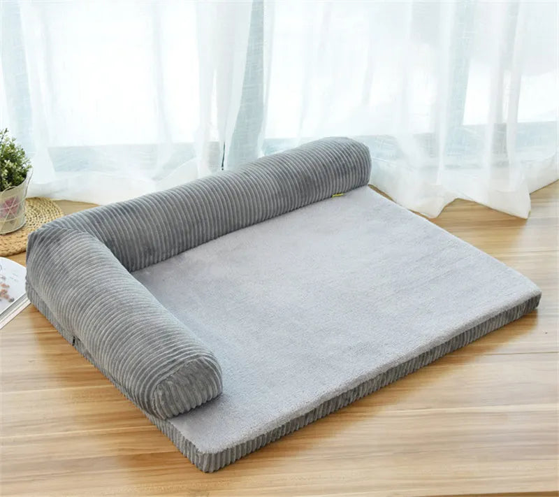 A corduroy pet sofa dog bed with a raised bolster, shown in a grey colour on a wooden floor.