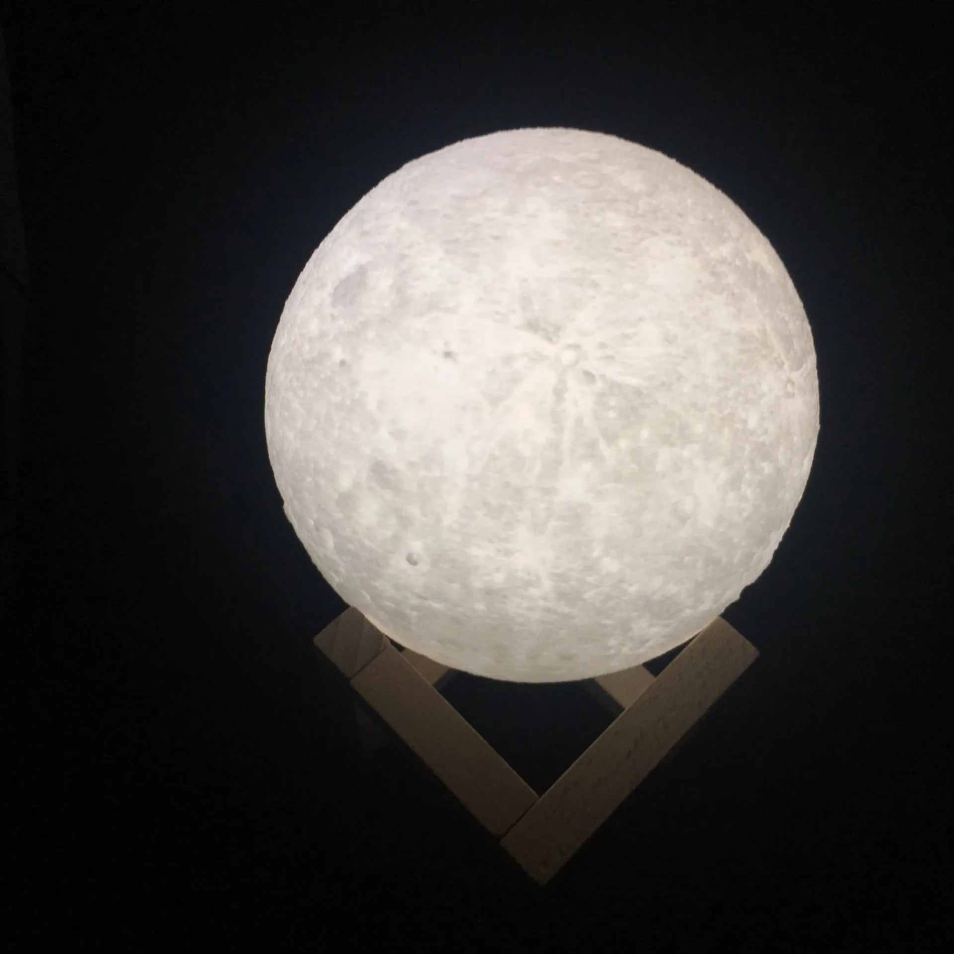 3D printed moon lamp glowing on a wood stand, showing detailed crater texture.
