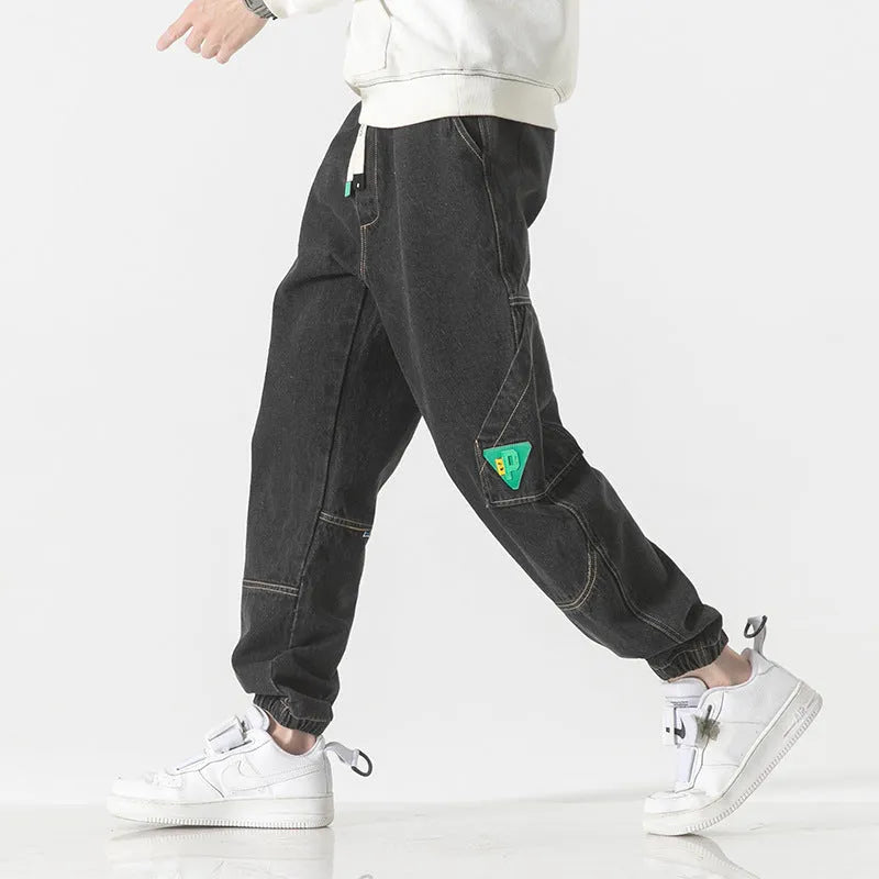 Men's black loose-fit tapered cotton trousers on a hanger, showing the mid-waist and tapered leg design.