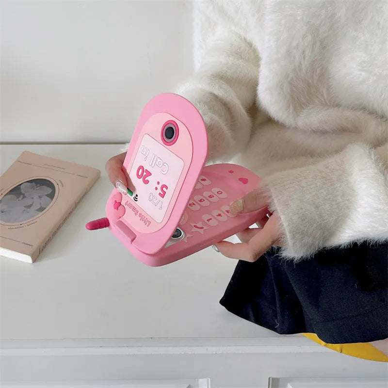 Pink silicone flip phone-shaped iPhone case with a built-in mirror and cute cartoon design.