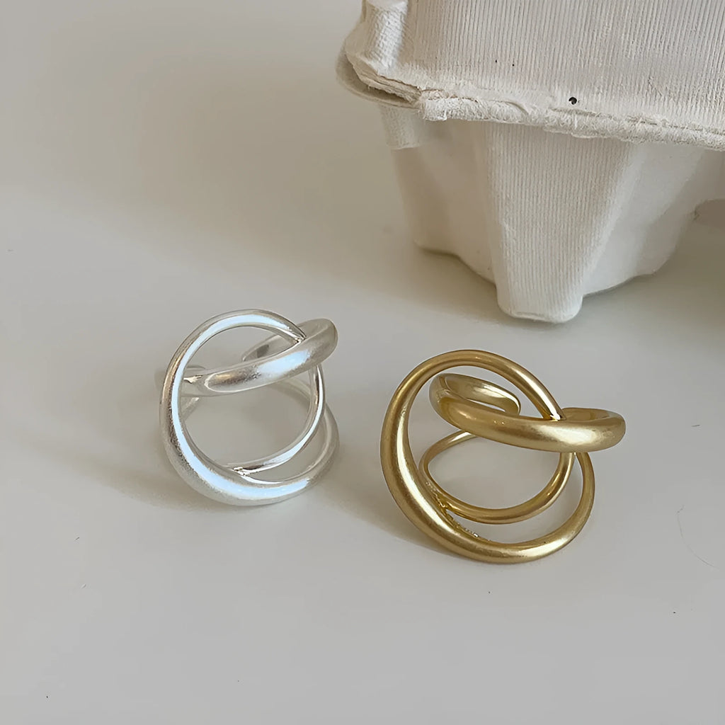 Matte metal open ring with three-dimensional interlaced geometric design in gold or silver finish.