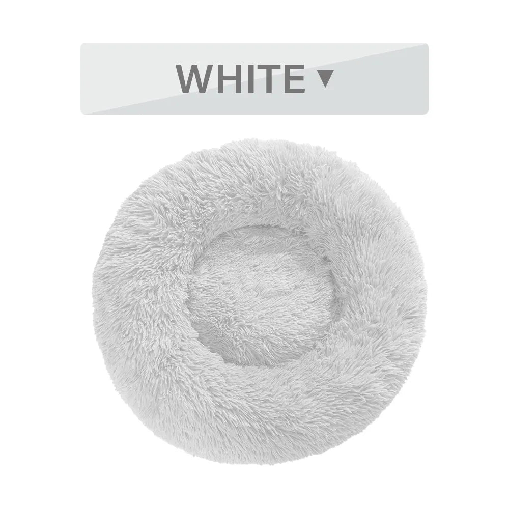 Fluffy donut-shaped dog bed in long plush material, shown in a light grey colour with a raised edge.