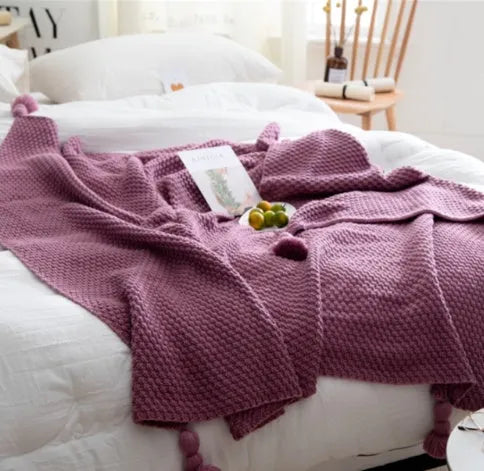 Acrylic knitted blanket with fringed edges in a neutral colour on a sofa.