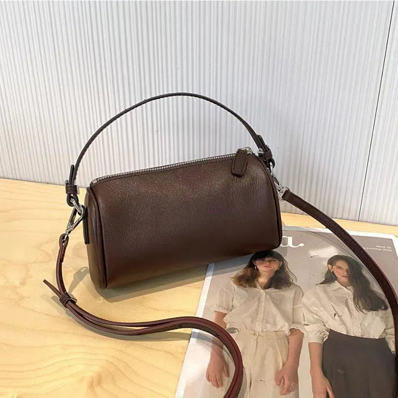 Vegetable-tanned leather crossbody phone bag with cylindrical shape and visible sewing thread detailing