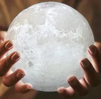 3D printed moon lamp glowing on a wood stand, showing detailed crater texture.