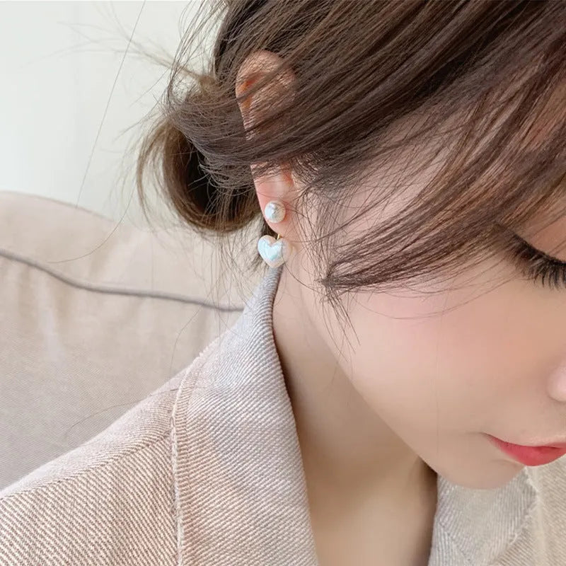 Korean style women's heart shaped stud earrings with pearl-like artificial gemstone inlay on a white background.