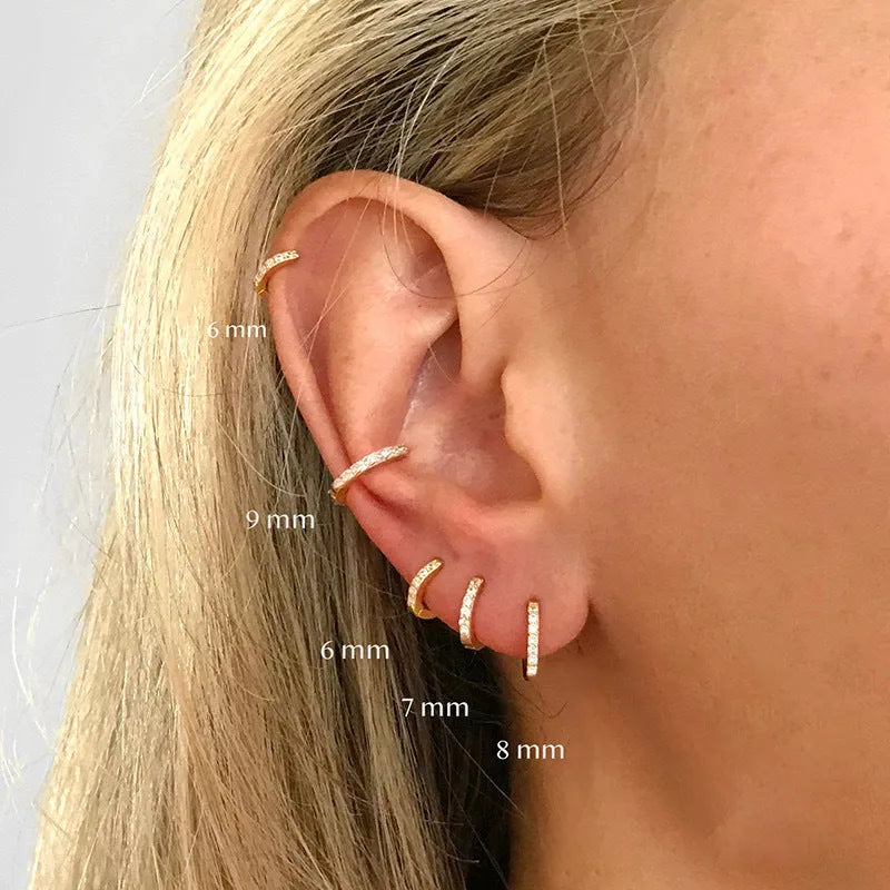 Gold, rose gold, and silver coloured geometric perforated circle stud earrings with zircon details on a white background.