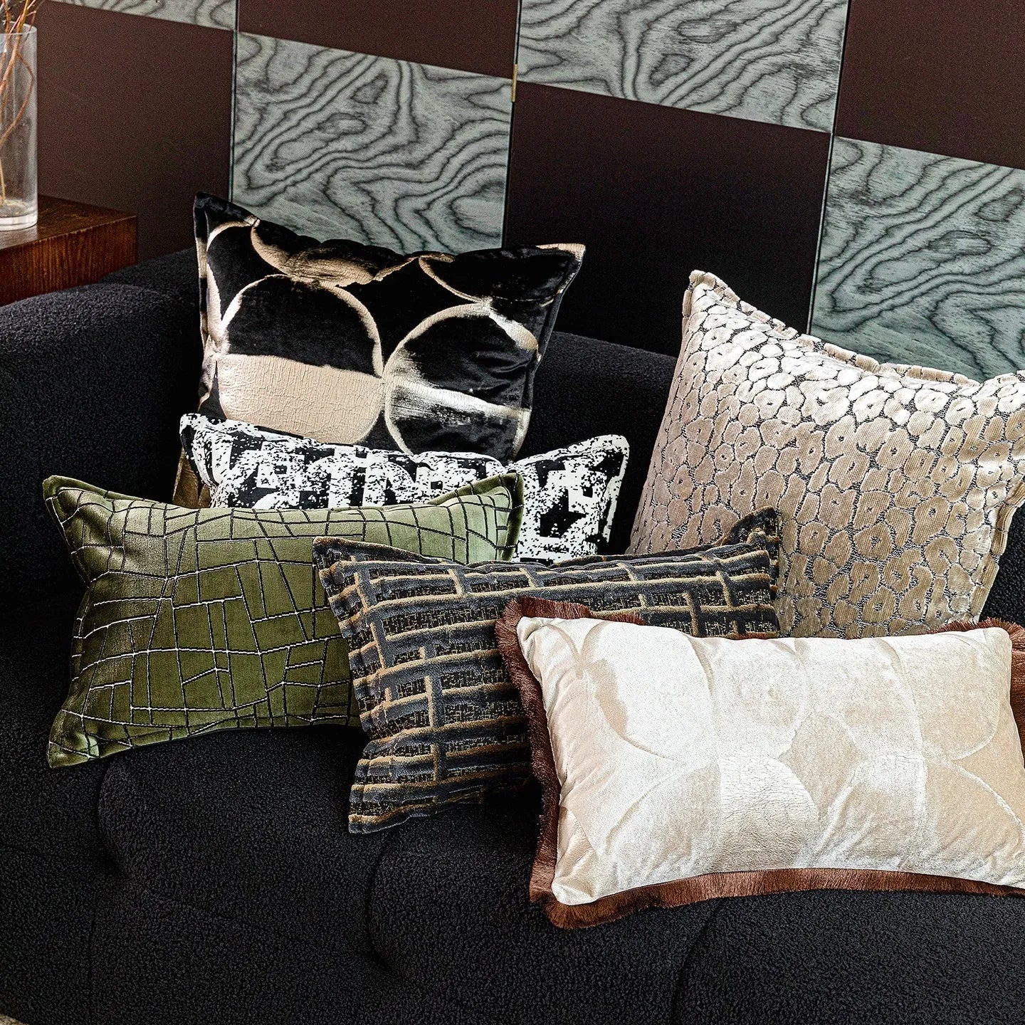 Black and gold abstract patterned flannel decorative pillow with removable cover on a grey sofa.
