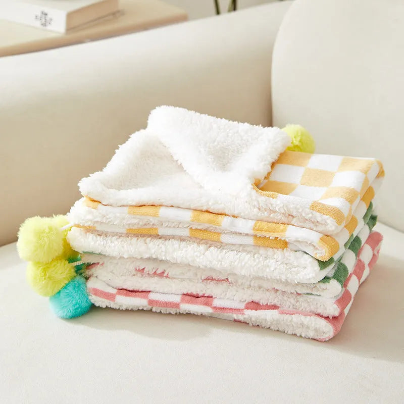 Green plaid pattern pet blanket with fur ball decoration on a sofa.