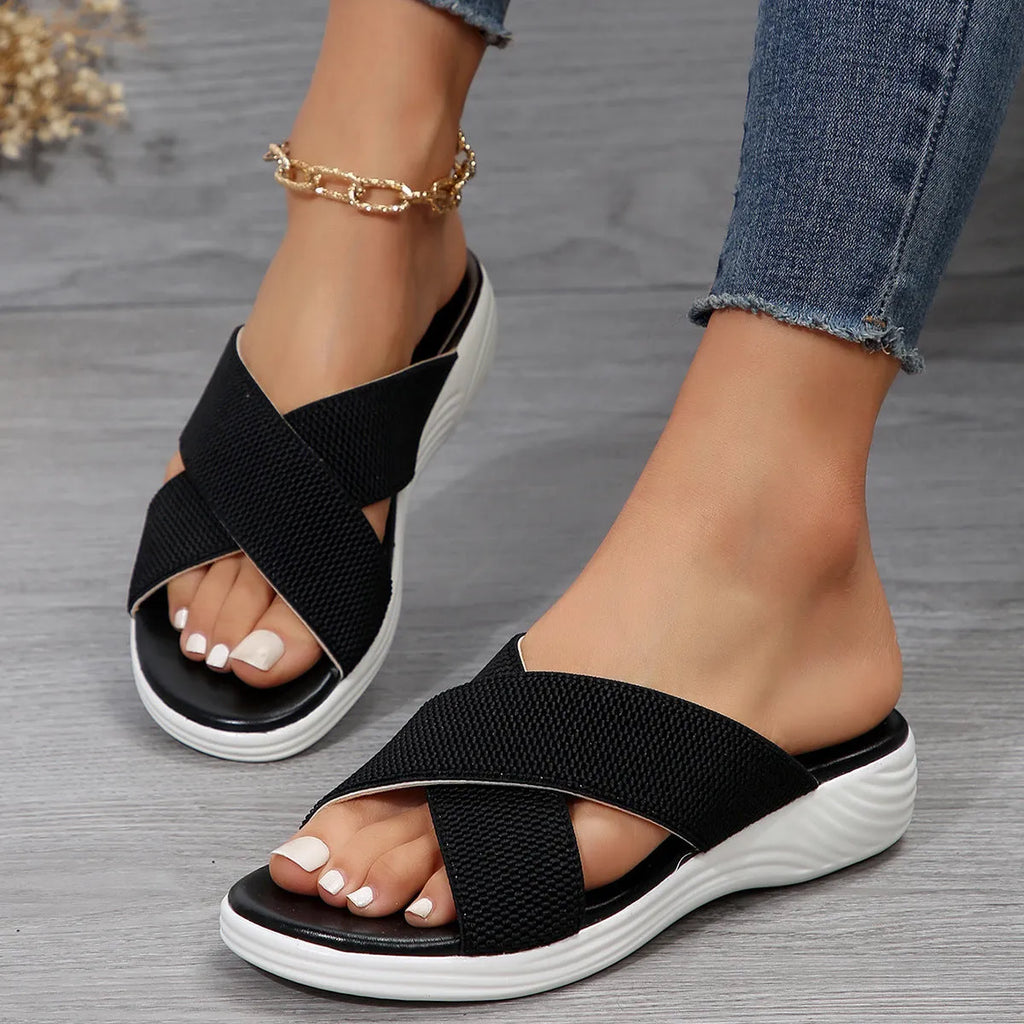 Black women's peep-toe wedge slippers with a thick rubber sole on a plain background.