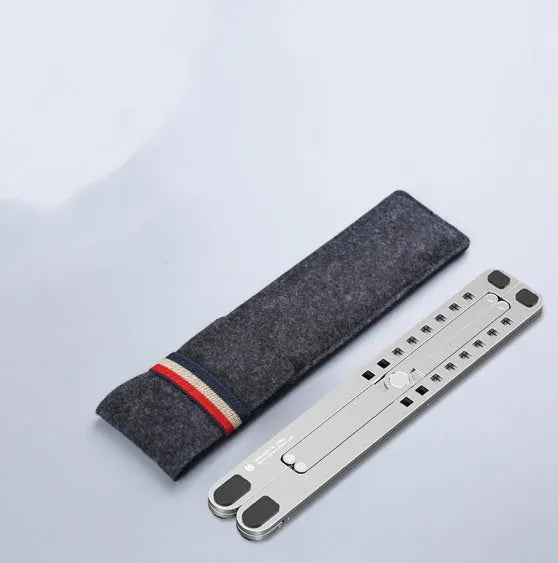 A folded aluminium laptop stand in silver next to an open laptop, demonstrating its compact size.