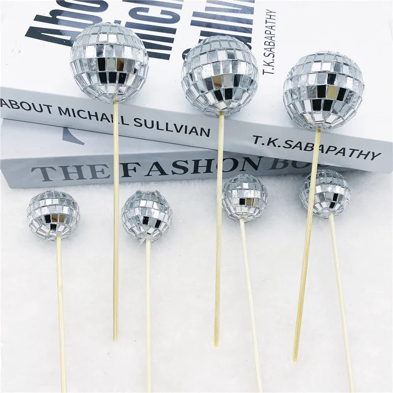 Silver reflective glass disco ball cake topper on a wooden stick for birthday party decoration.