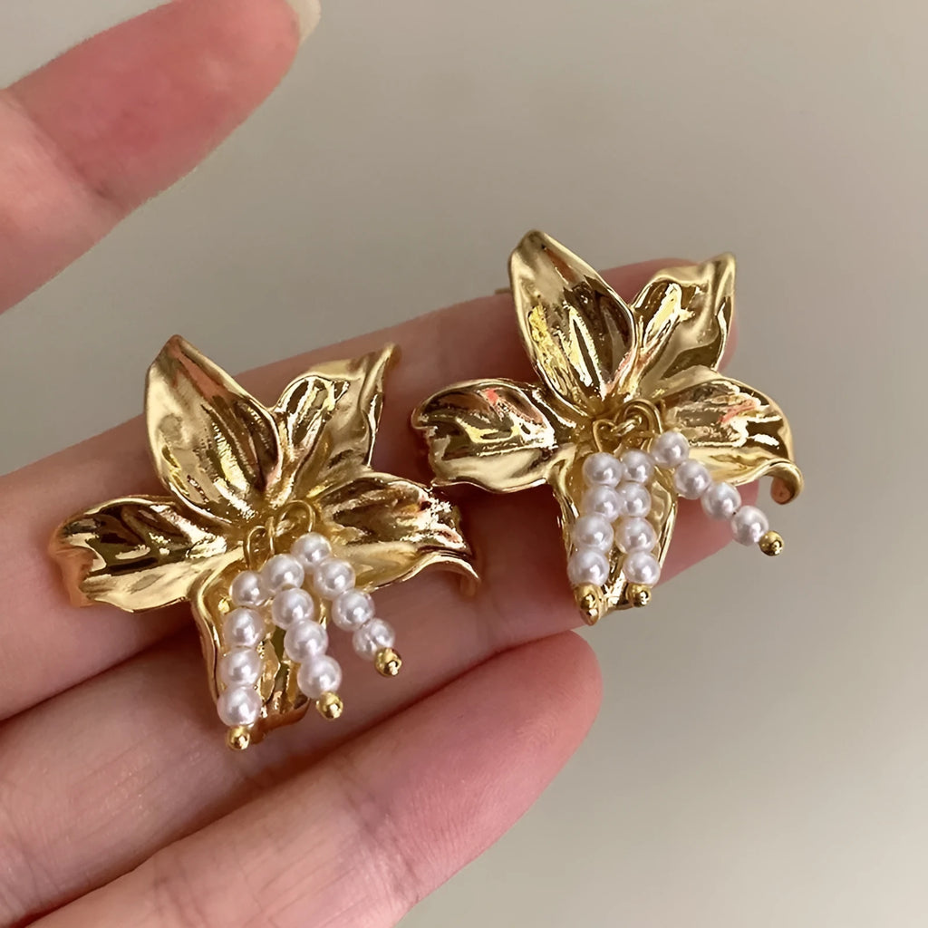 A pair of exaggerated gold metal flower earrings with pearls, showing niche style design.
