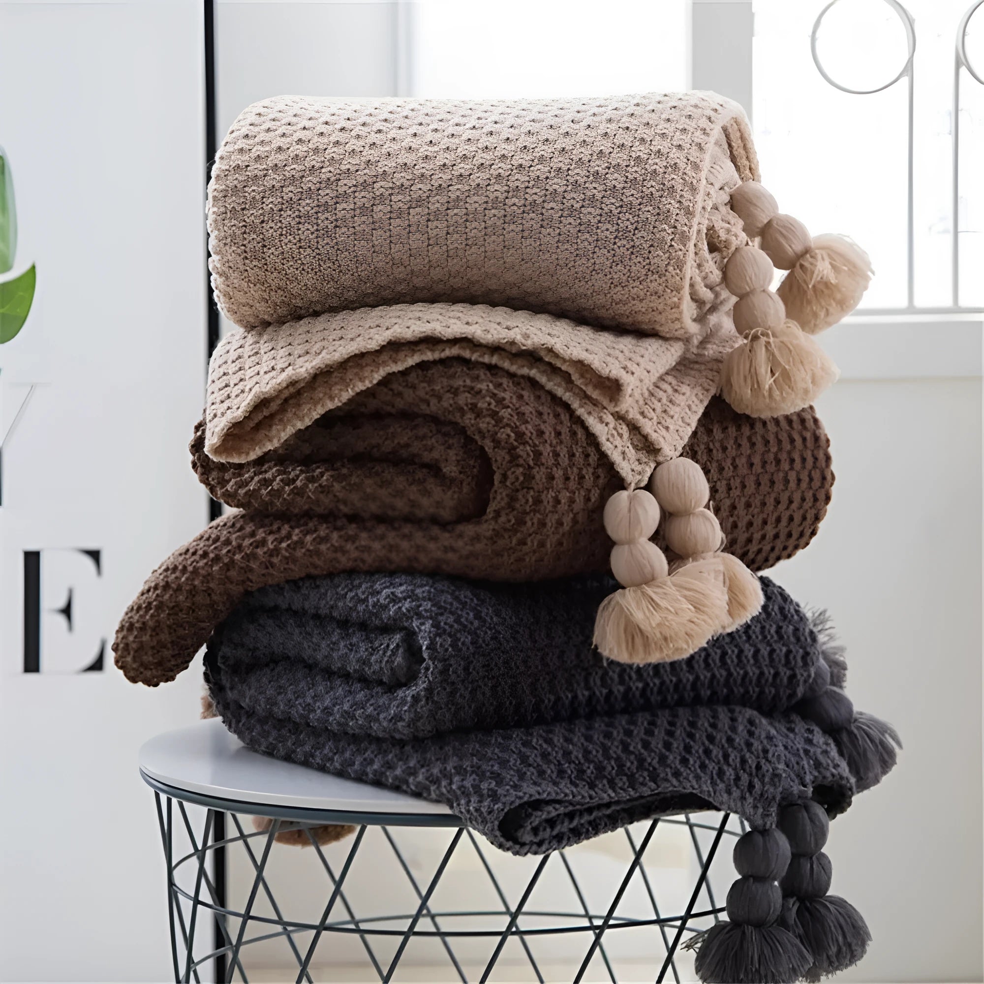Acrylic knitted blanket with fringed edges in a neutral colour on a sofa.