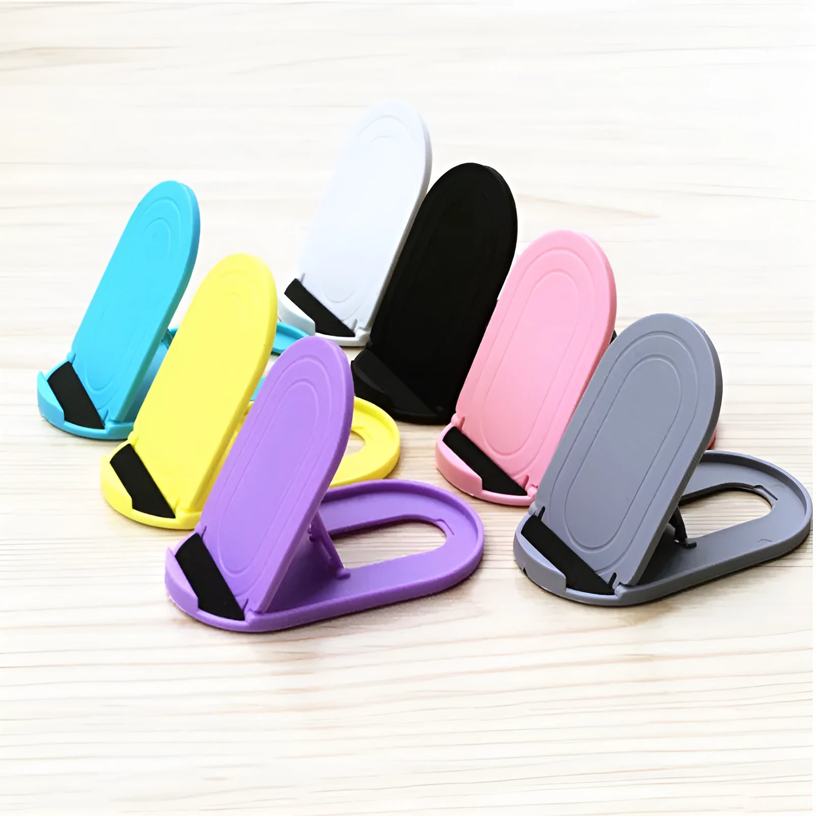 Plastic mobile phone stand with lazy bracket design in six colour options on a table.
