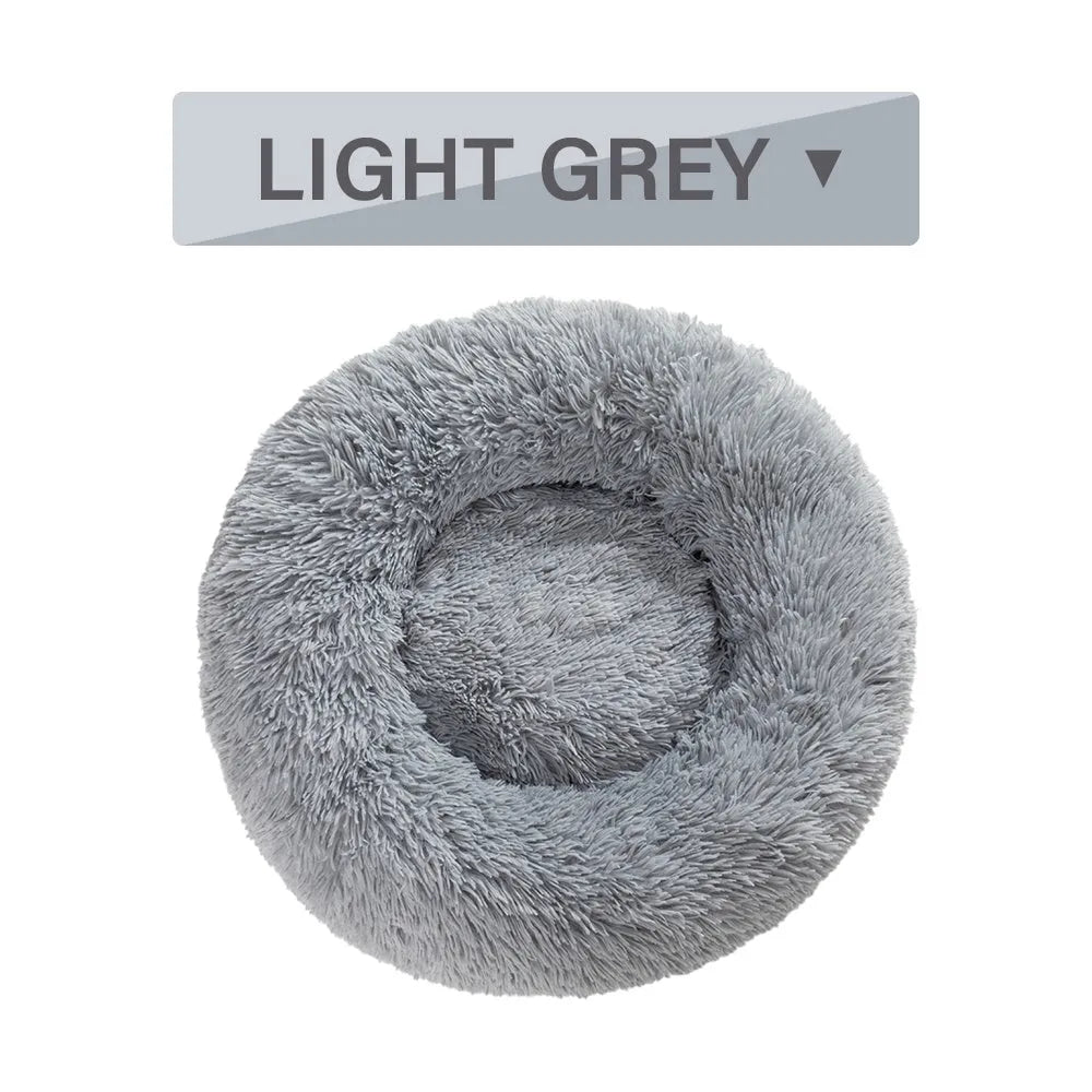 Fluffy donut-shaped dog bed in long plush material, shown in a light grey colour with a raised edge.