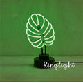 White bamboo-shaped desktop lamp with green light tube on a wooden desk.