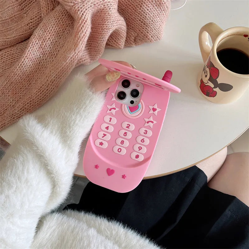 Pink silicone flip phone-shaped iPhone case with a built-in mirror and cute cartoon design.