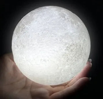 3D printed moon lamp glowing on a wood stand, showing detailed crater texture.
