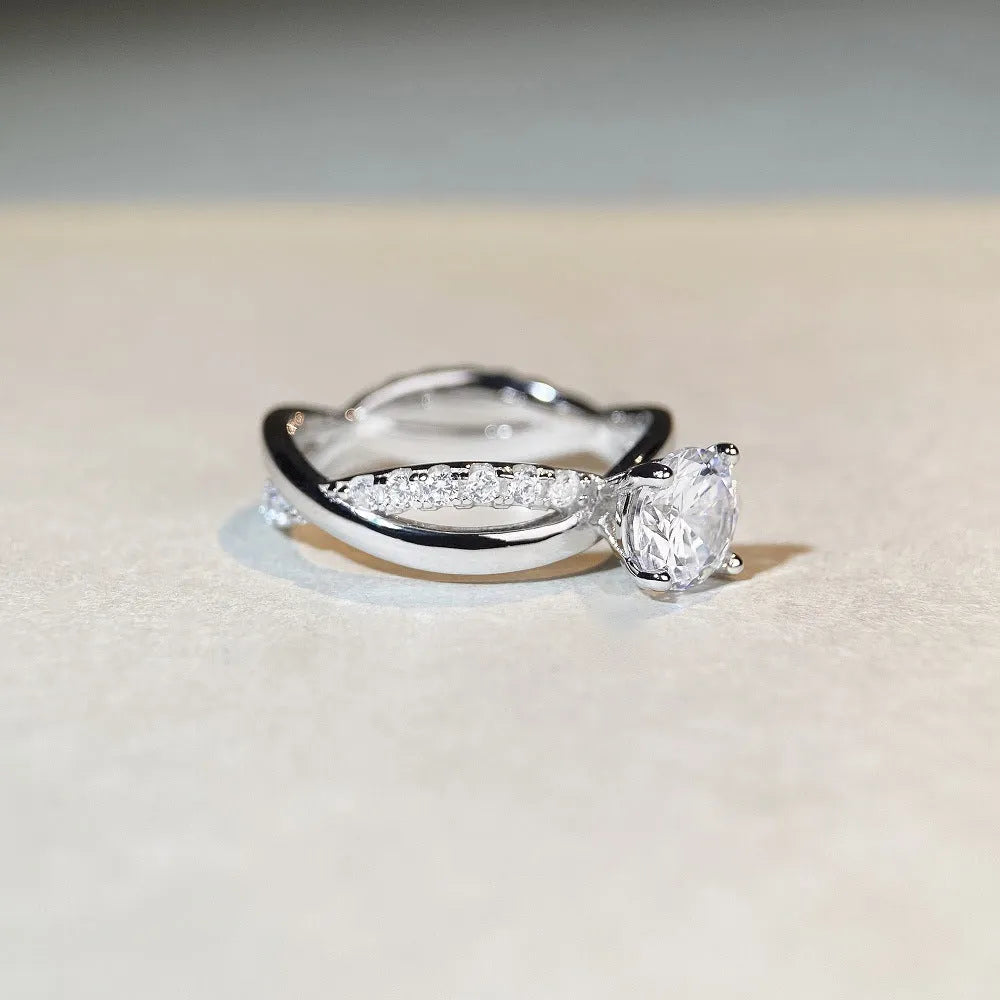 Silver geometric cross ring with a 1 karat moissanite stone in a four-claw setting on a twisted band.