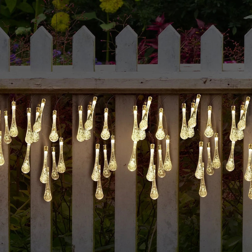 Solar-powered water drop LED string lights in garden with ground spike and bubble pendant design
