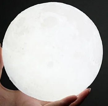 3D printed moon lamp glowing on a wood stand, showing detailed crater texture.