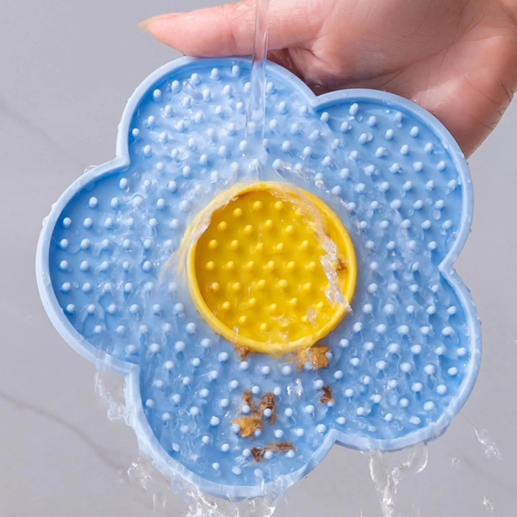 Flower-shaped blue silicone dog licking mat with suction cups on a smooth tile surface.
