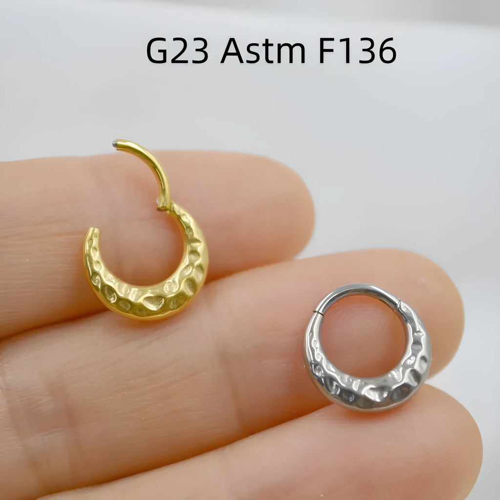 Close-up of a titanium alloy concave-convex nose ring in gold finish, showing carved detail and ring shape.