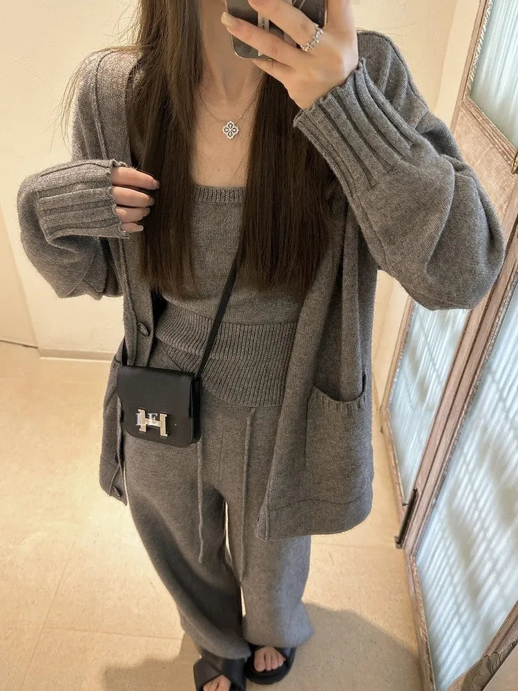 Women's beige knitted cardigan three-piece set with sleeveless vest and suspender trousers on a hanger.