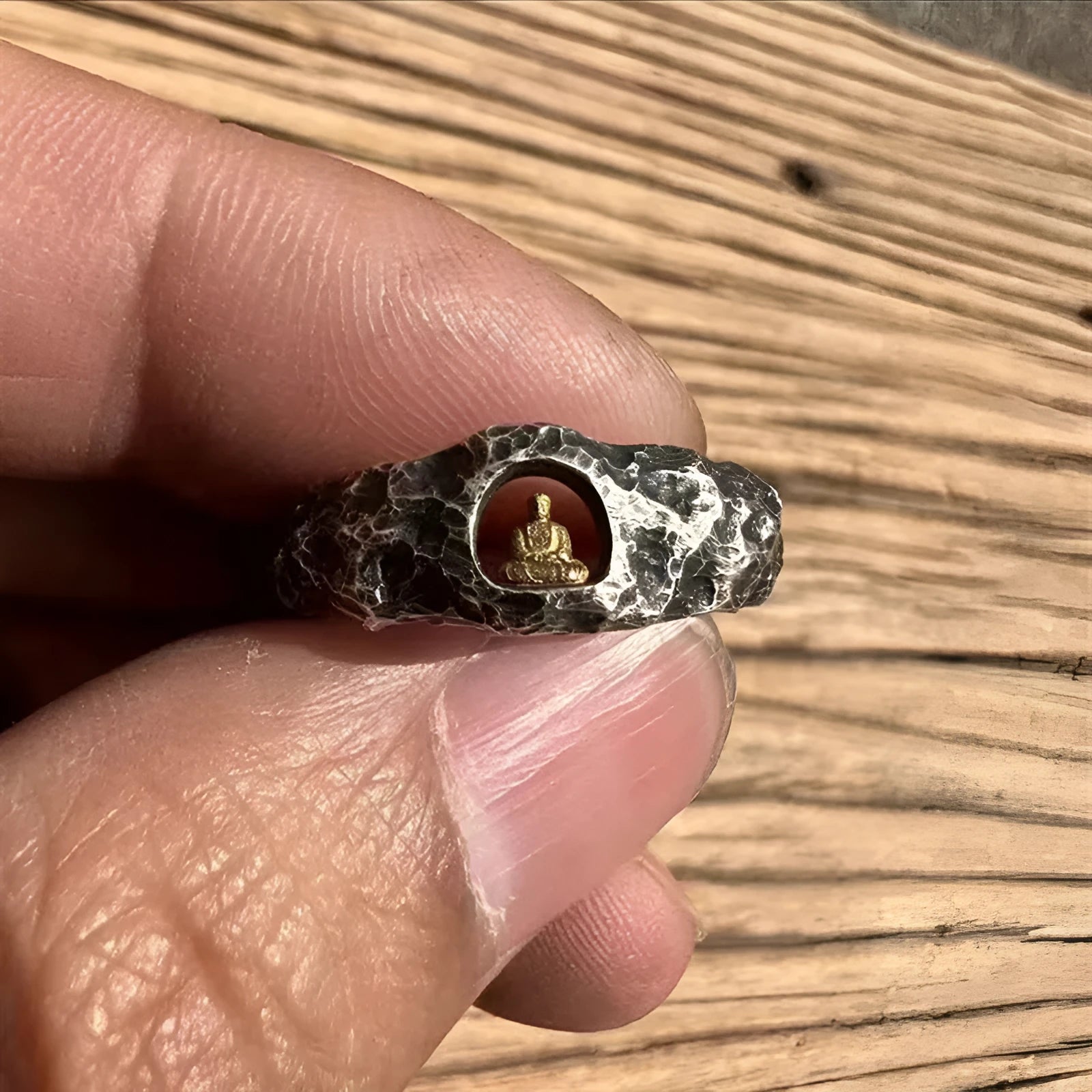 Close-up of a hand-forged copper ring with a rough rock texture and a detailed Buddha motif, shown on a finger.