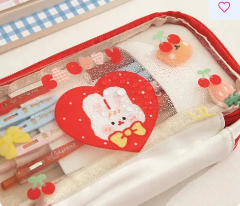 Transparent pink heart-shaped pen case with a cartoon cake and rabbit design, shown open.