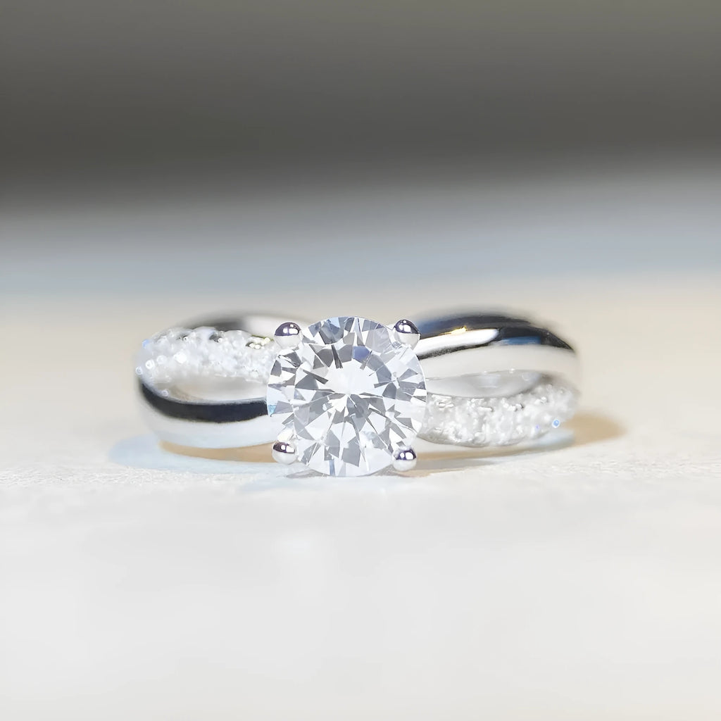 Silver geometric cross ring with a 1 karat moissanite stone in a four-claw setting on a twisted band.