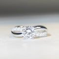 Silver geometric cross ring with a 1 karat moissanite stone in a four-claw setting on a twisted band.